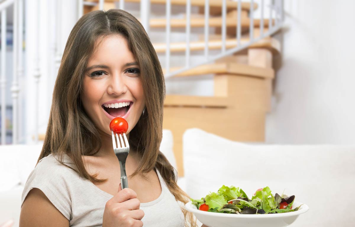 Woman eating a tomato with a bowl of salad