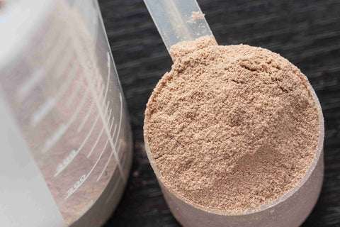 Scoop of chocolate protein powder beside a supplement tub